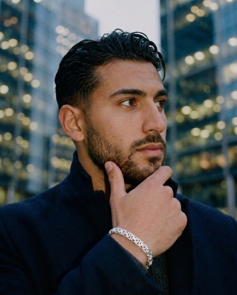 A man in a navy overcoat at dusk, hand to his chin, wearing the King&rsquo;s Byzantine solid silver bracelet